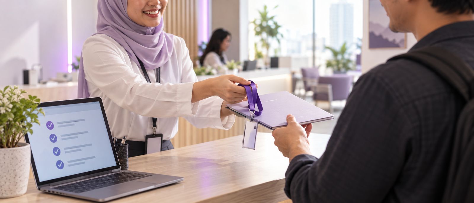 An HR officer handing a new employee a lanyard and onboarding folder beside a laptop showing a completed checklist