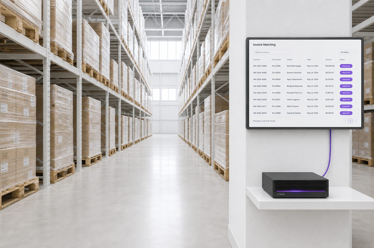 A warehouse aisle of stacked pallets with a wall-mounted terminal showing matched vendor invoices, fed by a local AI server on the shelf beneath it